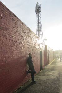 Leaning against the wall of the West Stand