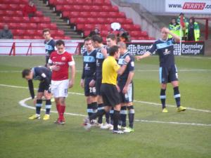 The referee sorts the wall out, before the free kick comes to nothing