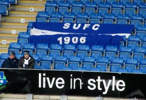 A couple of travelling supporters sit by a flag